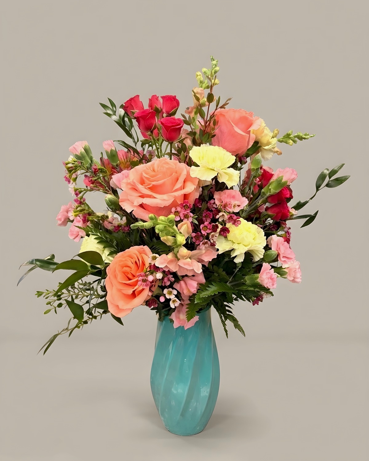 Coral roses and pink snapdragon in a turquoise glass vase