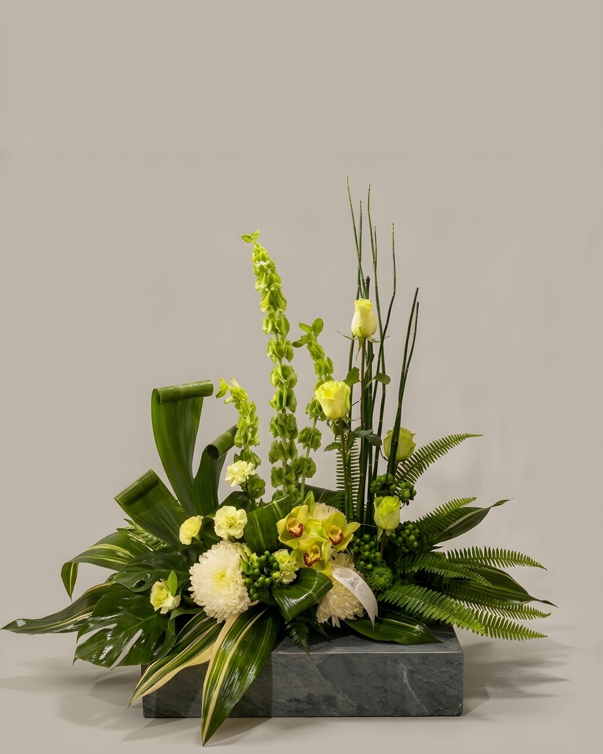 Low green and white centrepiece with ti leaf, bells of Ireland and white mums