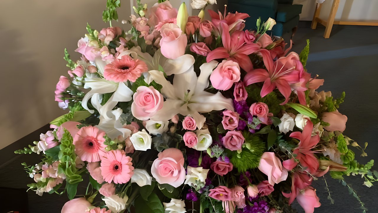 A casket spray built by Greenville Floral, with pink lilies, gerbera daisies and roses among white lilies and purple stock, set up in a funeral home.
