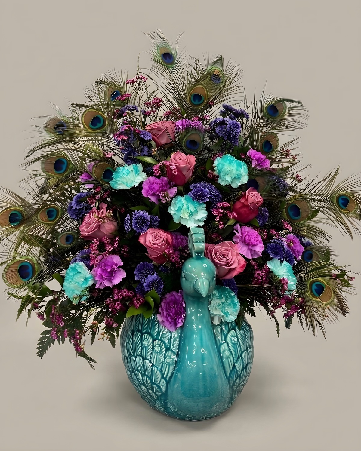Purple and teal carnations and roses with peacock feathers in a teal vase