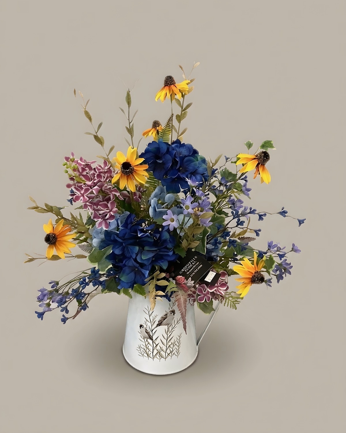 Black-eyed susans, blue delphinium and yellow blooms in a white ceramic pitcher