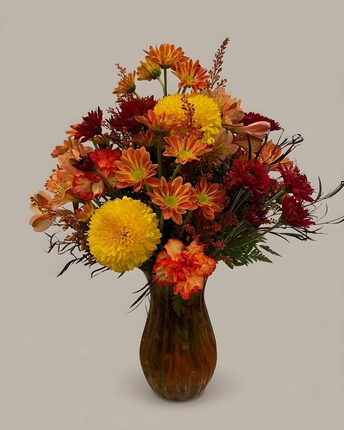 Rust chrysanthemums, orange gerberas and gold accents in a tall glass vase