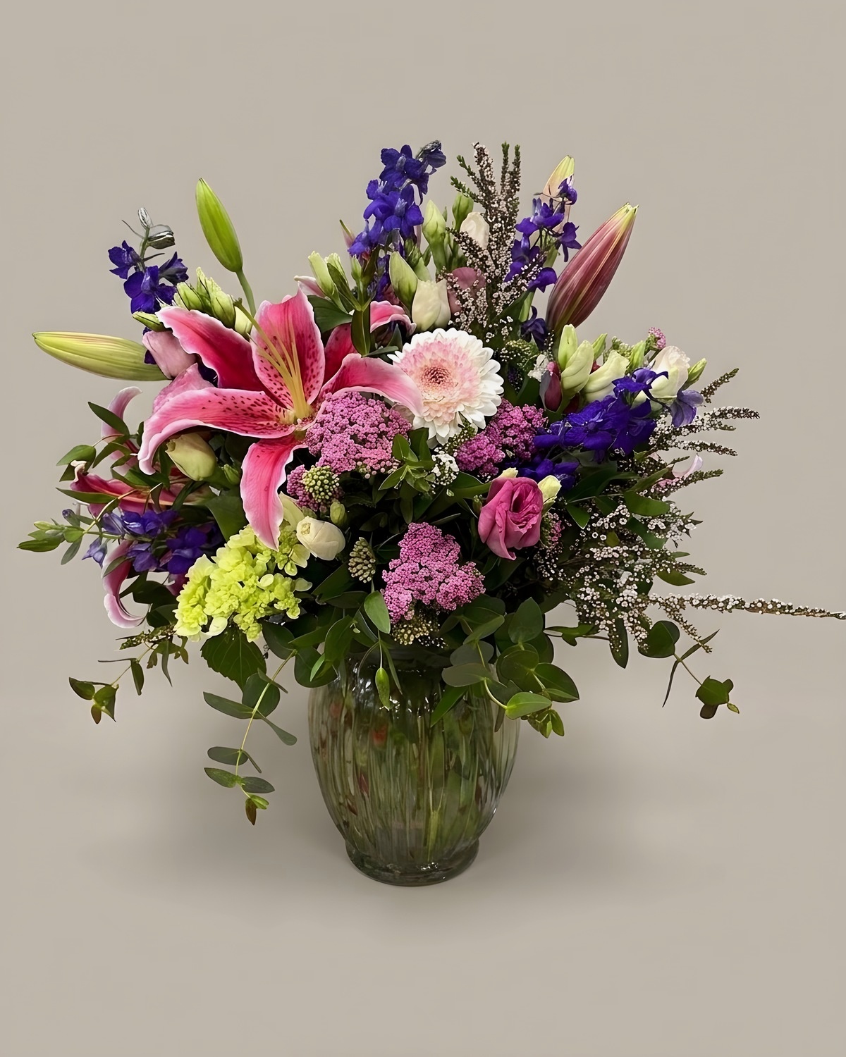 Pink stargazer lilies, purple delphinium and pink roses in a glass vase
