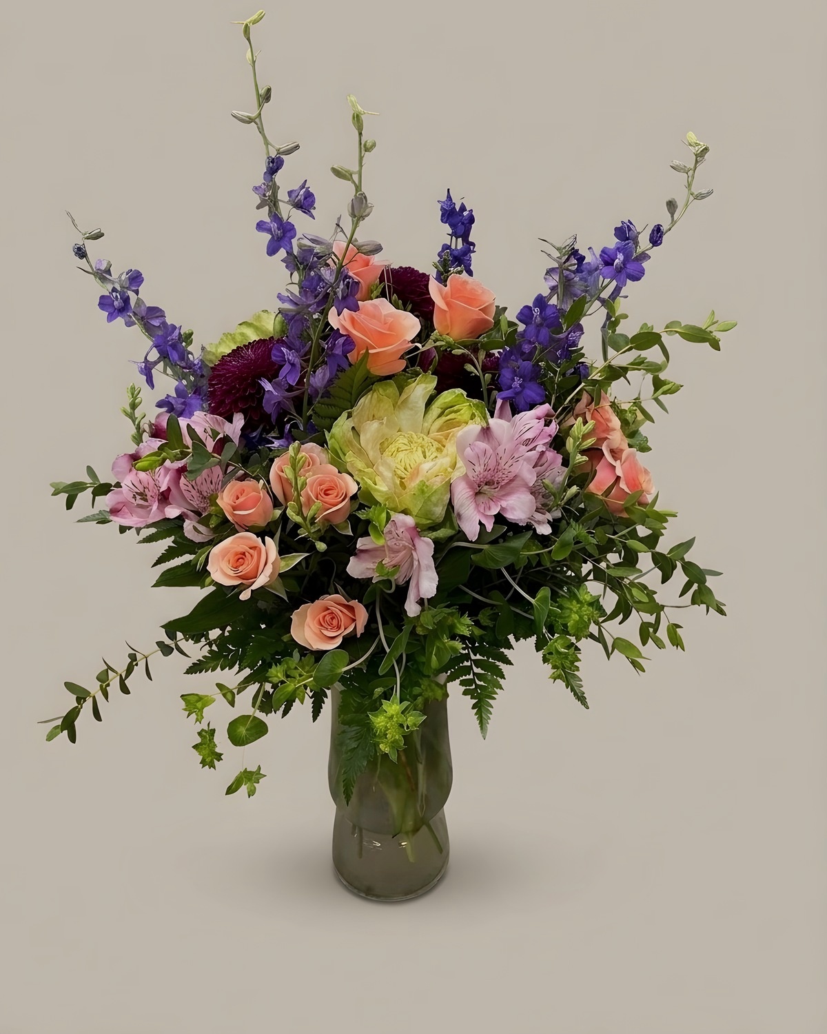 Peach roses, cream hydrangea and purple delphinium in a clear glass vase