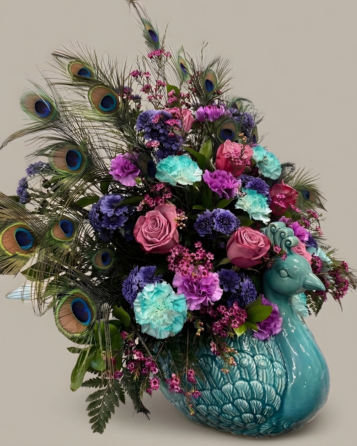 Purple and teal silk arrangement with peacock feathers in a teal ceramic peacock vase